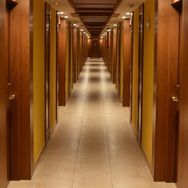 Long hallway view of a modern hotel with wooden doors and ceiling, creating a luxurious ambiance.